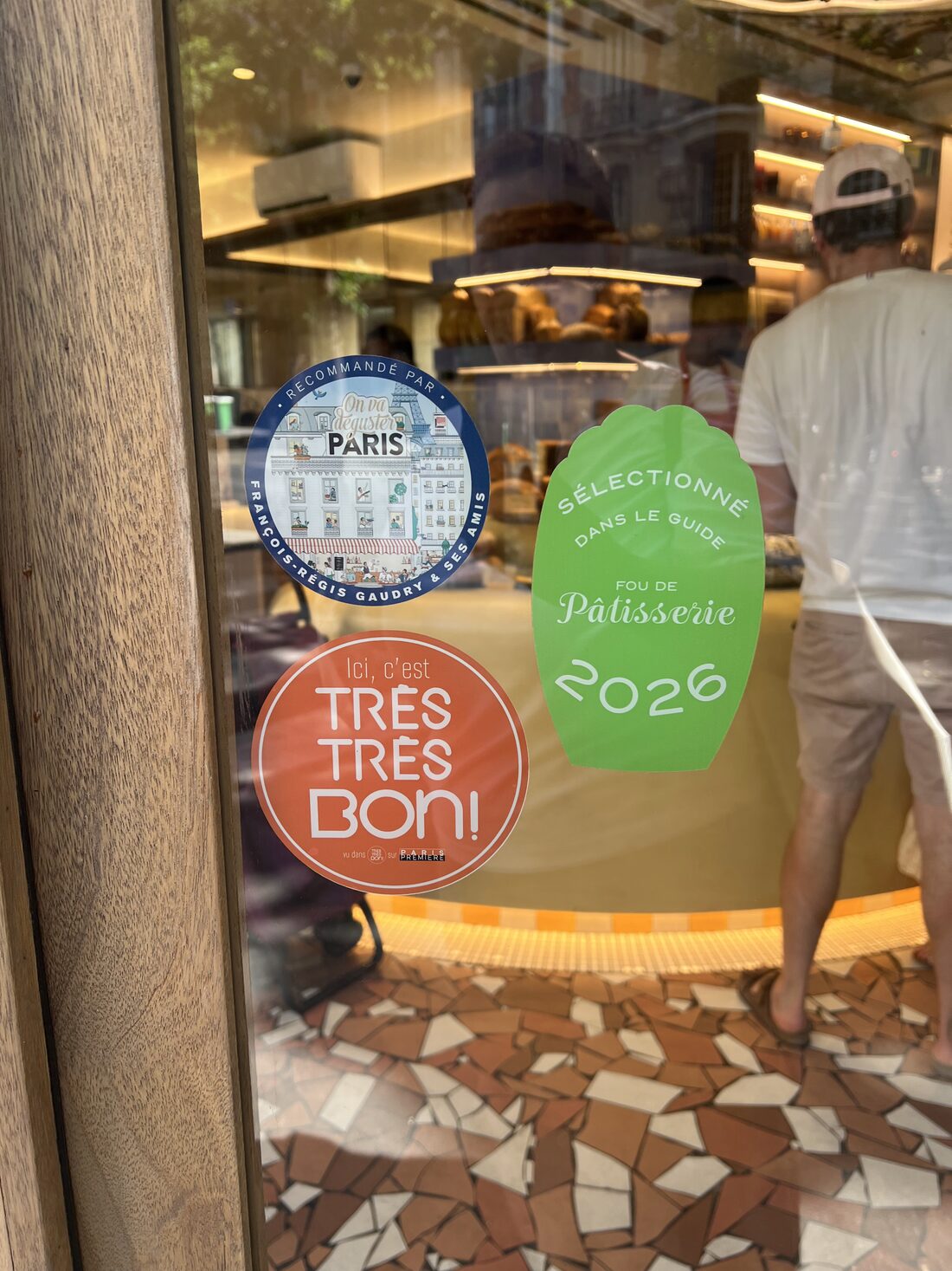 A Paris bakery window with award stickers: On va déguster Paris, Très Très Bon, and Fou de Pâtisserie 2026