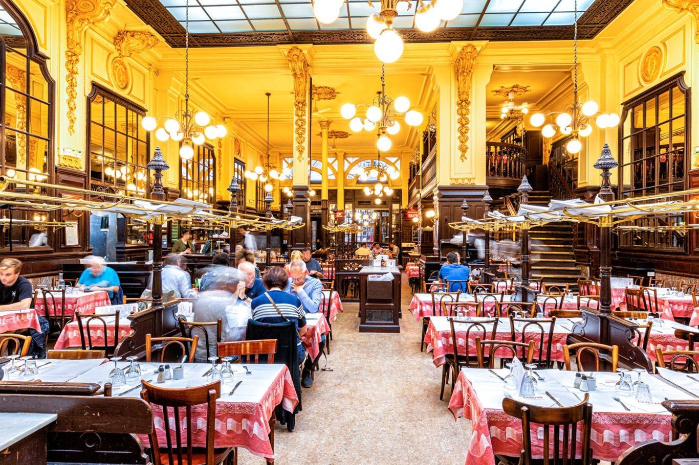 The grand dining room of a classic Paris bouillon — red-checked tablecloths, brass and mirrors, families eating