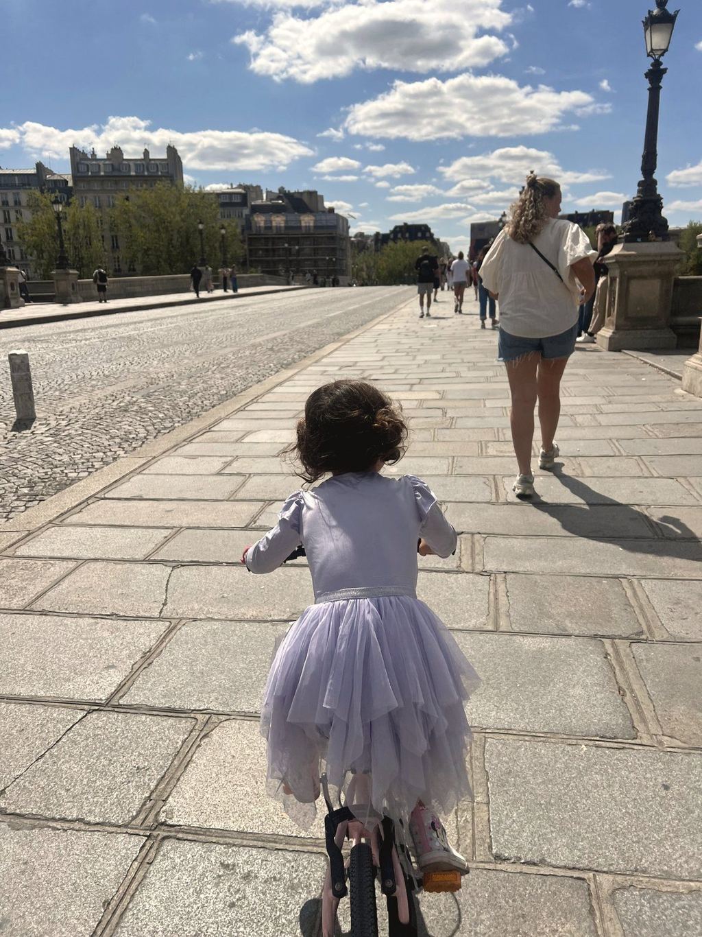 A child in a lavender tutu riding a bike on a Paris street, seen from behind