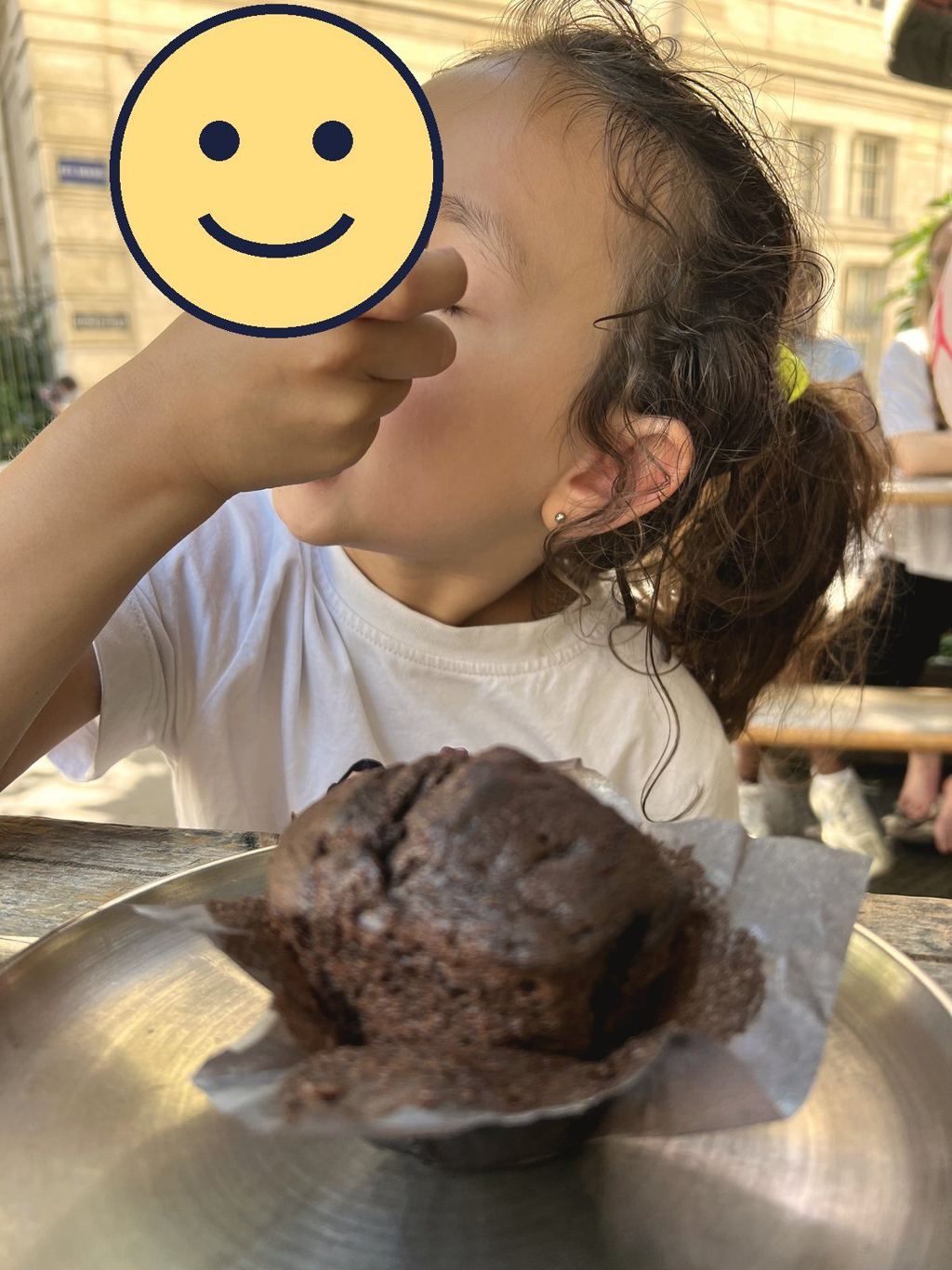 A child enjoys a chocolate muffin for goûter at an outdoor café table in Paris