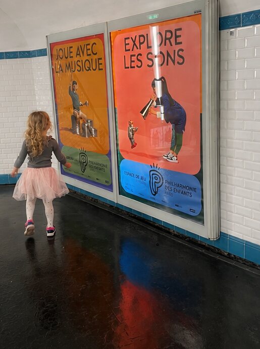 A child in front of bright Philharmonie des Enfants posters reading Joue avec la musique and Explore les sons