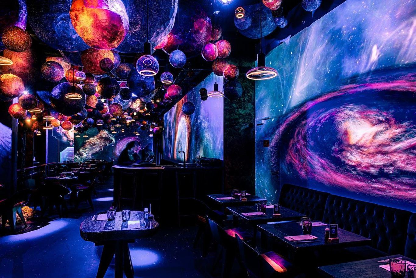The immersive space-themed dining room at Stellar, Paris — planets and a galaxy projected across the walls and ceiling